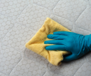 main dans un gant bleu qui essuie un matelas avec un chiffon